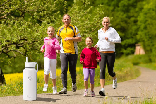 SmartFlask white insulated stainless steel water bottle with straw lid placed on a park trail, featuring a family jogging in the background—perfect hydration for active Australian families.